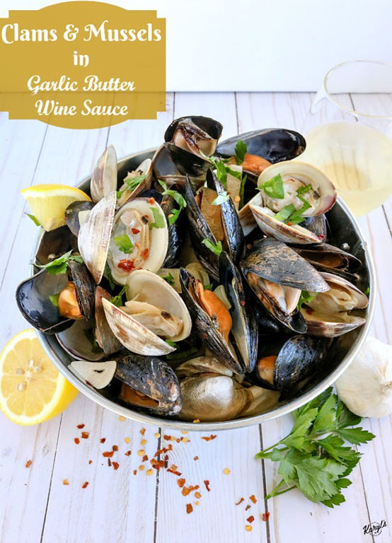picture of clams and mussels in metal bucket, with lemons, garlic, parsley & red pepper flakes on table and glass of wine in backgriound