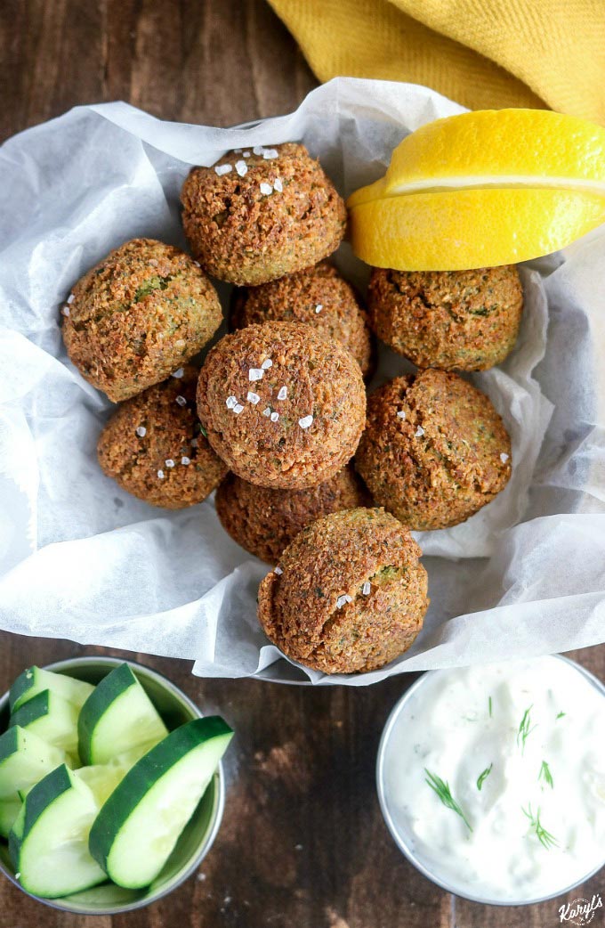 overhead shot of finished Falafel in a parchment-paper lined bowl, with cucumber wedges and Tzatziki sauce on the side
