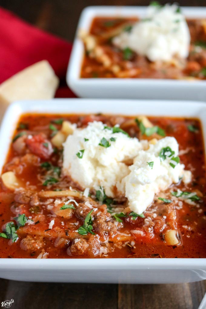 close up angeled shot of 2 white bowls filled with venison lasagna soup and topped with ricotta mixture