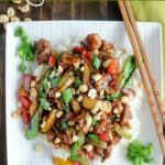 overhead shot of finished Kung Pao Chicken on a white plate with chopsticks on the right side of the plate