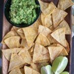 overhead shot of a plate of baked tortilla chips with guacamole and limes on the side