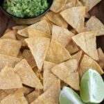 close up shot of baked tortilla chips with lime and guacamole on the side