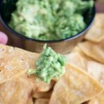 close up shot of baked tortilla chips with guacamole on one chip
