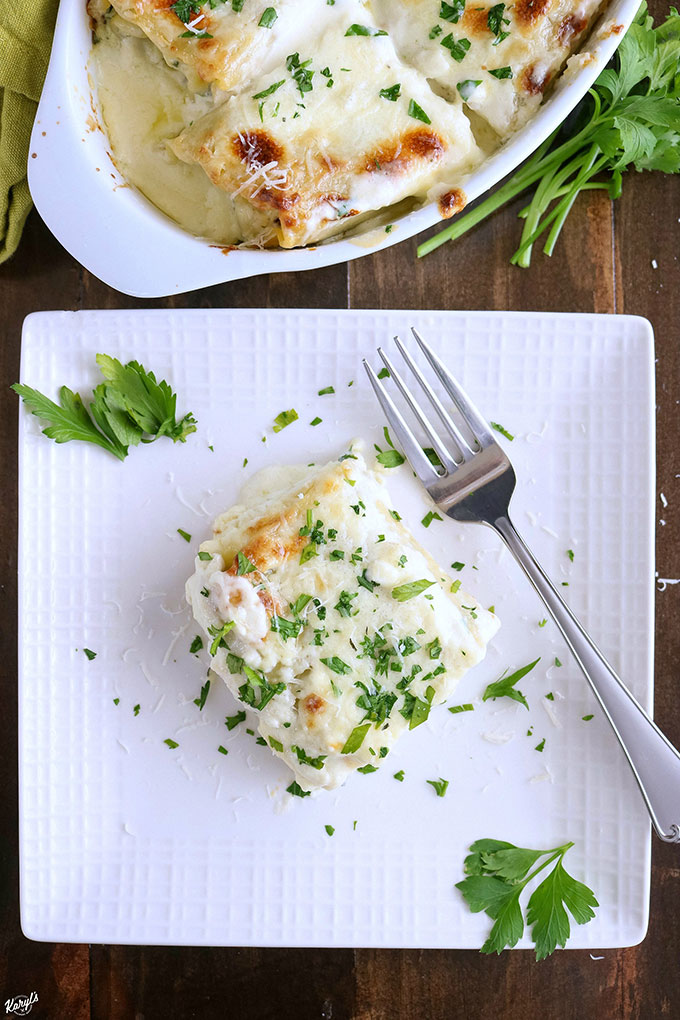 overhead shot of spinach alfredo lasagna roll ups on a white plate, garnished with parsley, with a fork on the plate