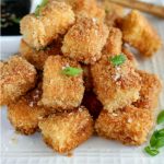 close up shot of a pile of finished Crispy Pan Fried Tofu on a white plate with chopsticks in the background