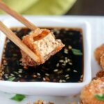 close up shot of a piece of Pan-Fried Tofu with a bite out of it over dipping sauce