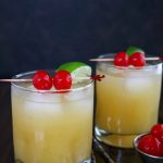 close up shot of 2 finished cocktails garnished with cherries and limes, with lime wedges on the side