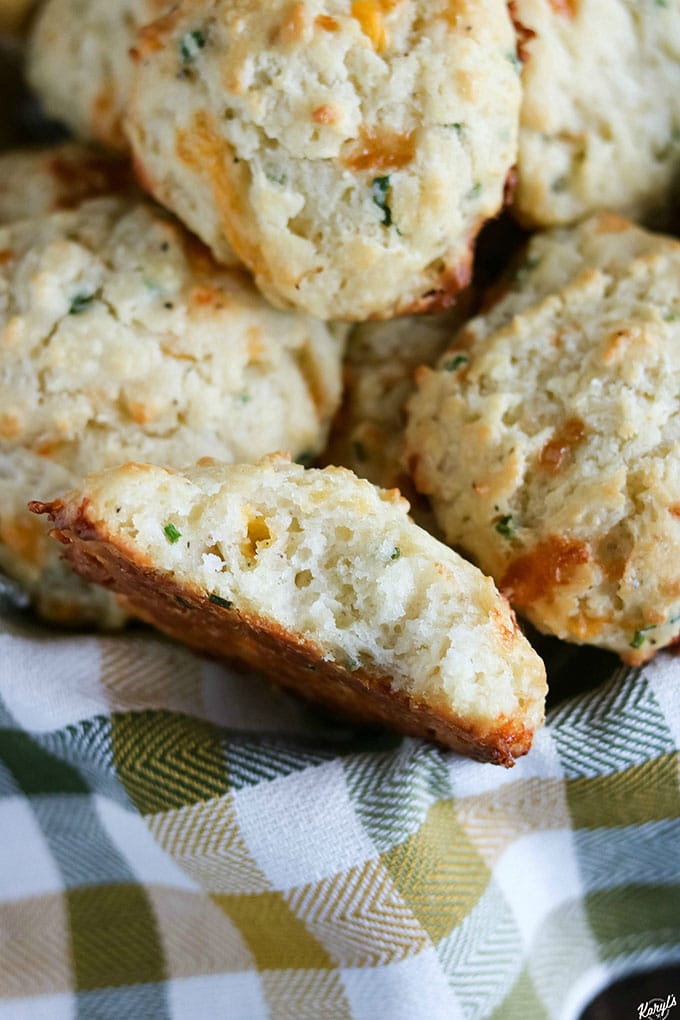 up close shot of Cheddar Chive Drop Biscuits in basket, with one biscuit cut open