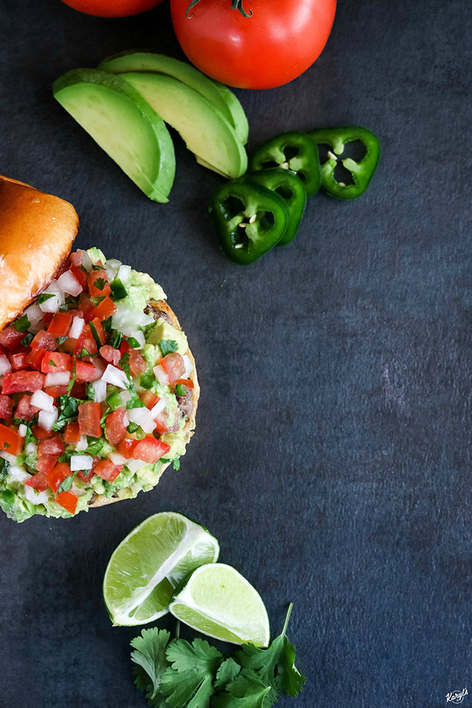 open faced burger off to the left hand side, with avocado and jalapeno in top corner, lime wedges in bottom corner