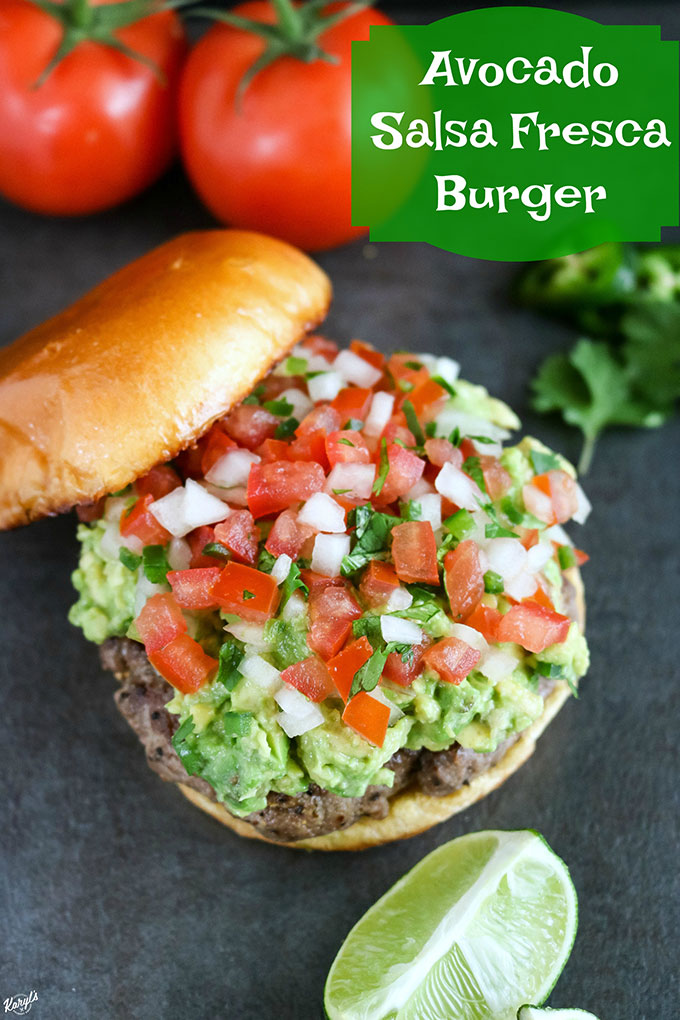 overhead shot of Avocado Salsa Fresca Burger with tomatoes in top corner and lime wedge in bottom corner