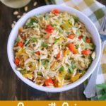 overhead shot of finished orzo with onion, garlic & peppers in a white bowl with a glass of wine on the side