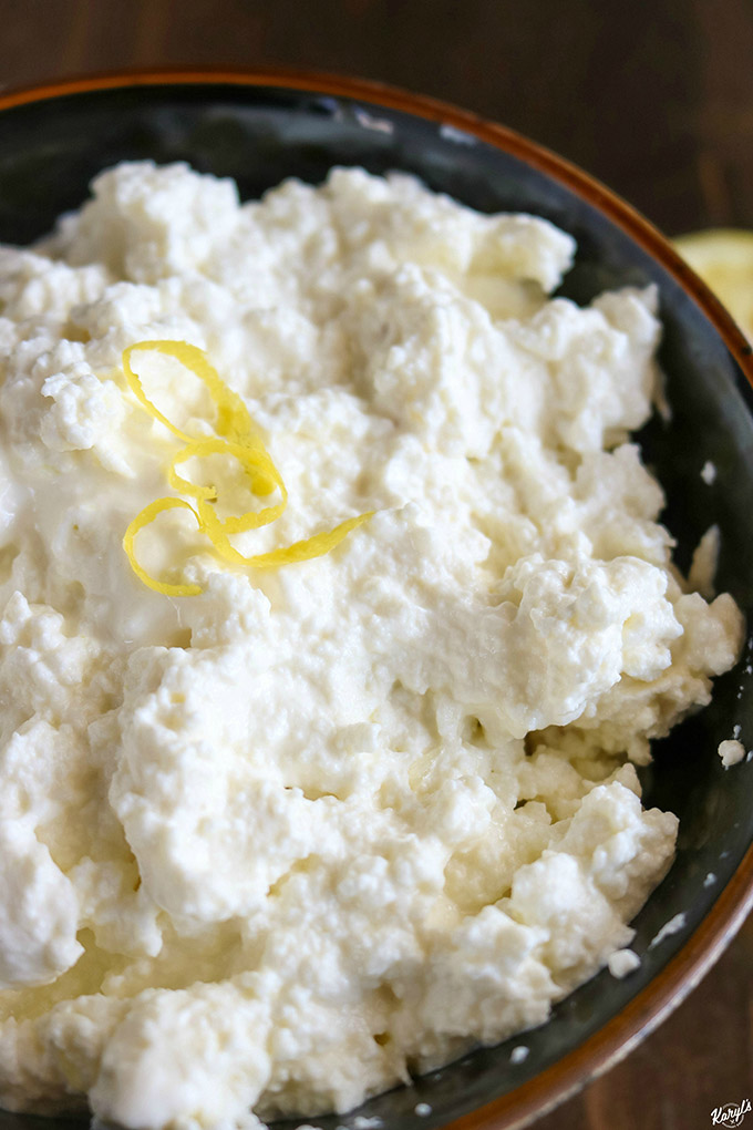 up close shot of ricotta in a black bowl, with a few lemon peel strips on top
