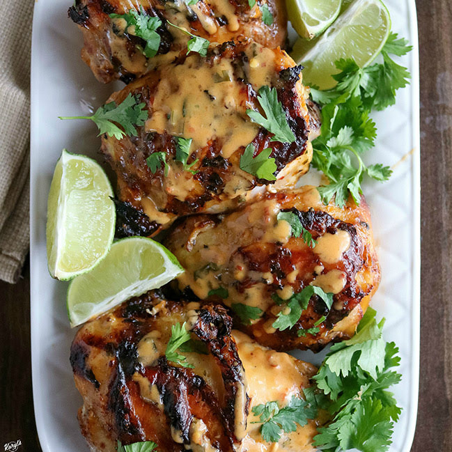 overhead shot of finished grilled chicken on a white platter with limes and cilantro garnish