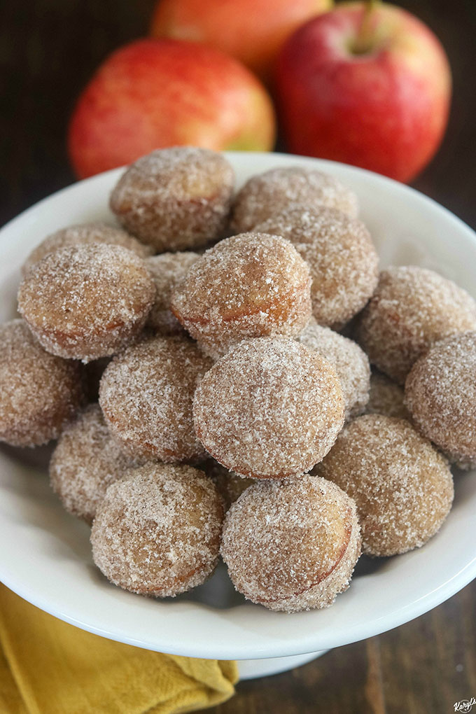 close up shot of finished apple cider donut holes on a white platter with apples in the background
