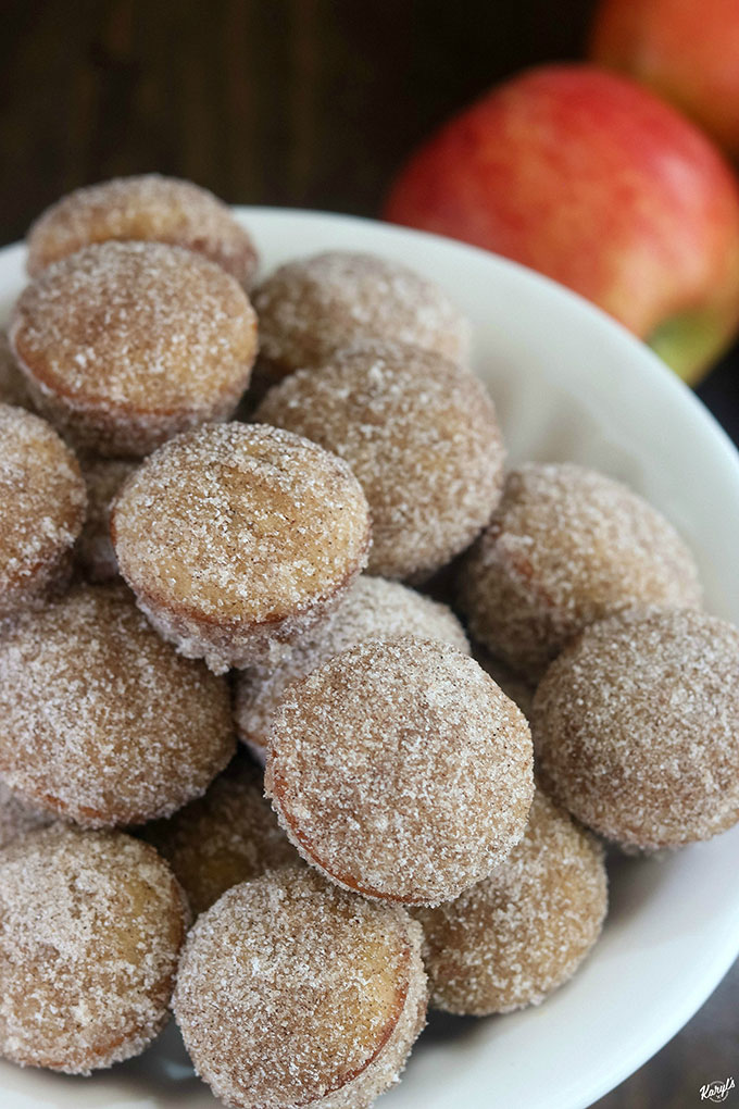 close up shot of finished apple cider donut holes on a white platter with apples in the background