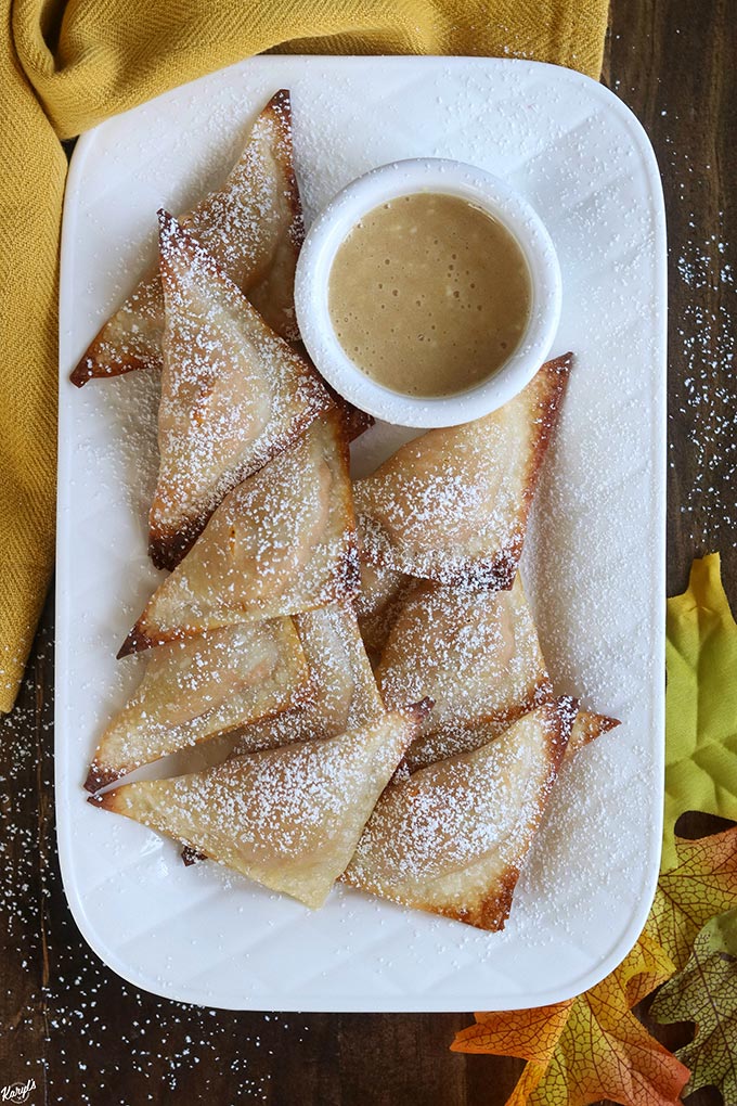 overhead shot of finished baked wontons on a white plate with a bowl of dipping sauce