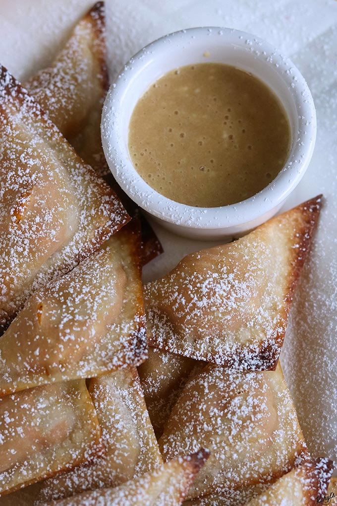 up close shot of finished baked wontons on a white plate with dipping sauce on the side