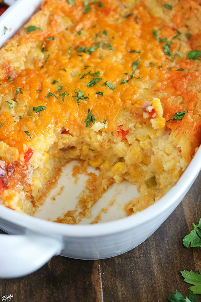 close up shot of finished corn casserole in a white baking dish with a piece cut out