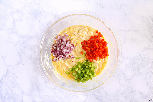 overhead process shot: corn mixture combined, with red and green bell peppers plus red onion on top