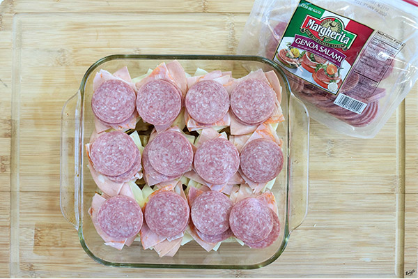 overhead process shot: olive spread, cheeses and meats layered on top of slider buns