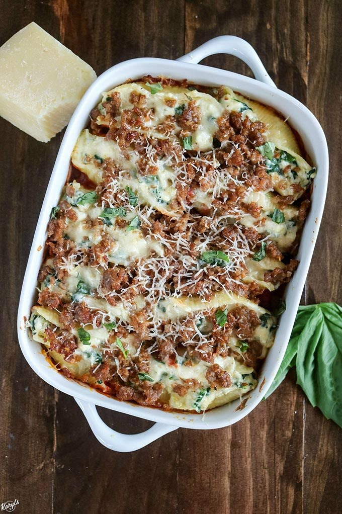 Overhead shot of finished Sausage Spinach Artichoke Stuffed Shells in a baking dish with a block of Parmigiano Reggiano cheese on the left