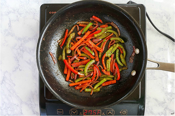 overhead process shot: onion and bell peppers in a black skillet, seasoned and sauteed until softened