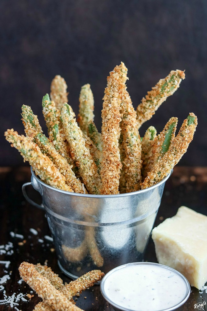 Close up shot of finished green bean fries in a metal bucket with a side of dipping sauce