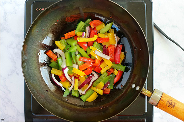 overhead process shot: bell peppers and onions added to oil and red pepper flakes in a black wok