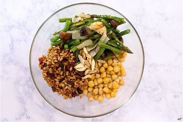 Process picture: overhead hot of chickpeas, farro, vegetables and sliced almonds in a glass bowl