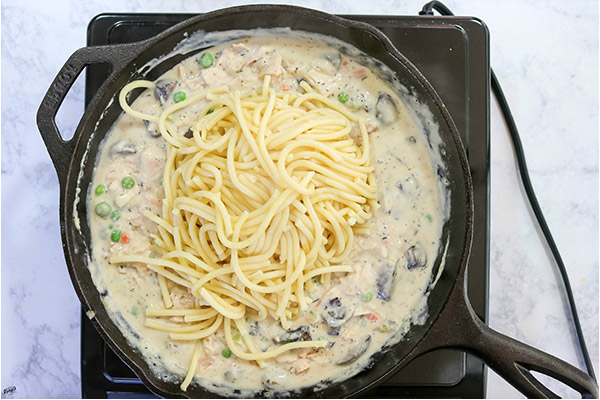 overhead process shot: pasta added to mixture in a black skillet