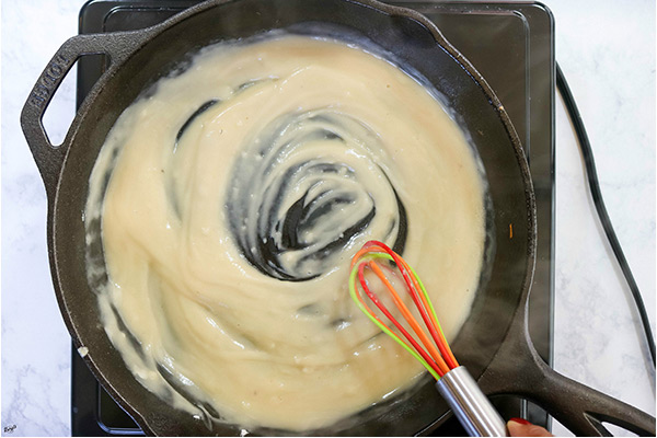 overhead process shot: melted butter and flour roux in a black skillet with a whisk