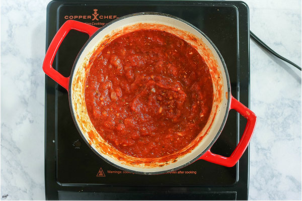 overhead process shot: onion, garlic, broth and all tomatoes simmering in a Dutch oven