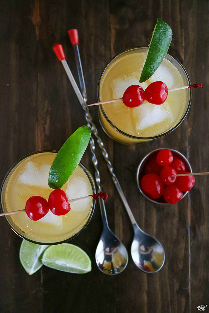 overhead shot of 2 Black Eyed Susans with 2 spoon in the middle with cherries and lime wedges on the side