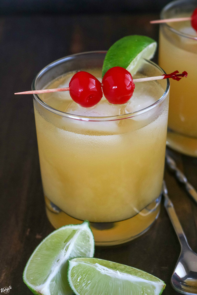 glass of Black Eyed Susan, garnished with 2 Maraschino cherries and a lime wedge close up shot of one cocktail in a short glass, garnished with cherries and lime with lime wedges on the side