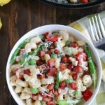overhead shot of a bowl of lemon ricotta fiesta pasta in a white bowl with a fork and napkin on the side with a skillet with more pasta in the background