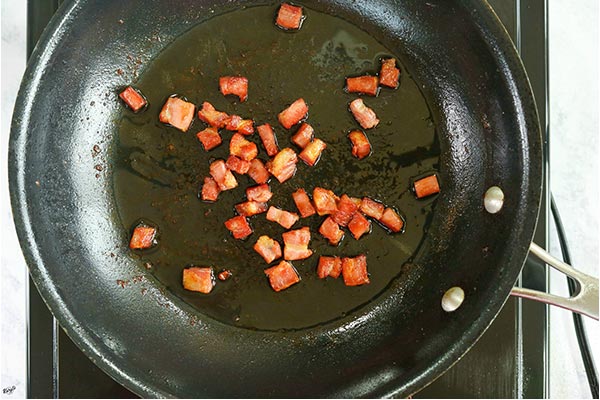 overhead process shot of pancetta cooking in a black skillet