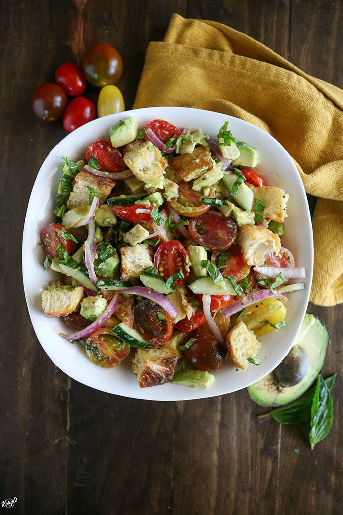 overhead shot of finished panzanella salad in a white bowl with avocado and tomatoes on the side