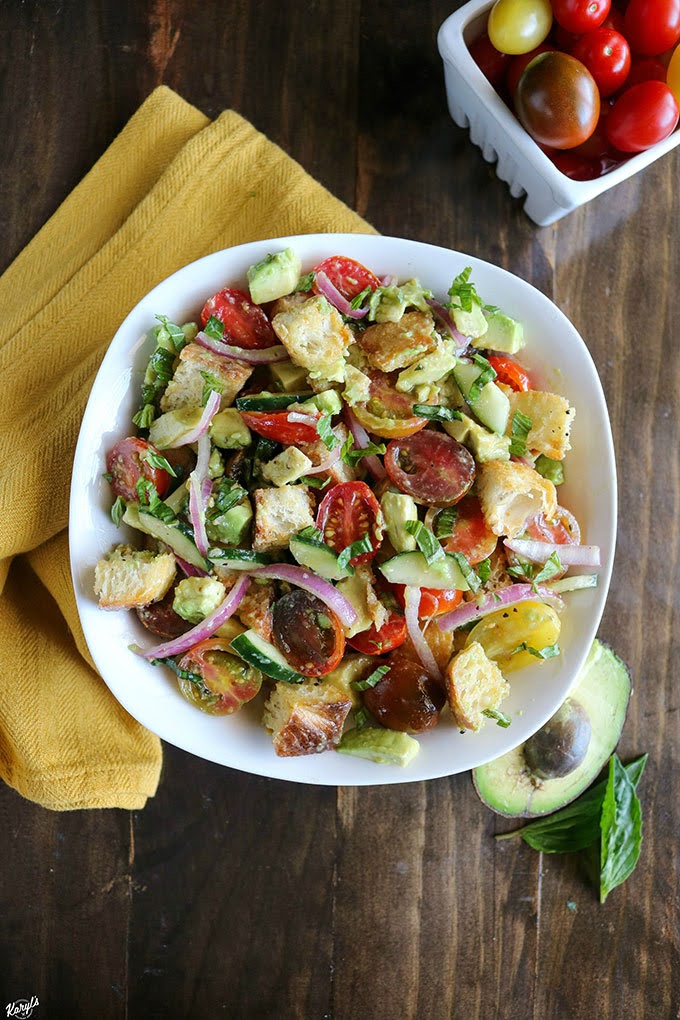 overhead shot of finished panzanella salad in a white bowl with avocado and tomatoes on the side