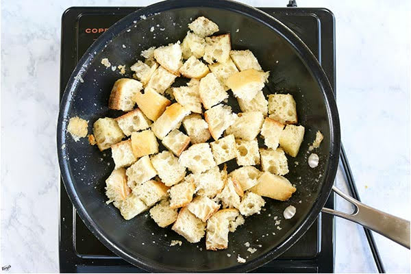 overhead process shot: cubed bread in a black skillet with melted butter