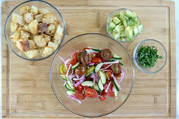 overhead process shot: large bowl of vegetables, plus smaller bowls of bread, avocado and basil