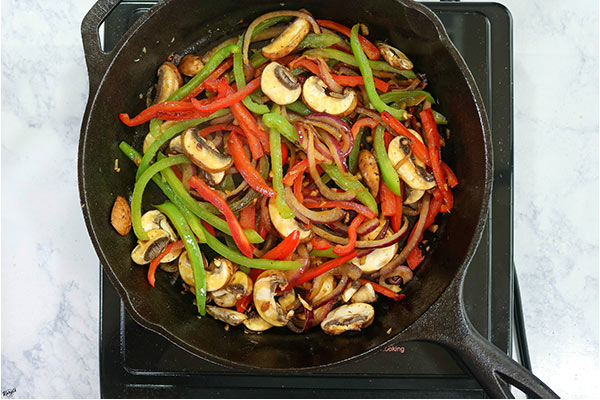 Overhead process shot: peppers, onions and mushrooms cooking in a cast iron skillet